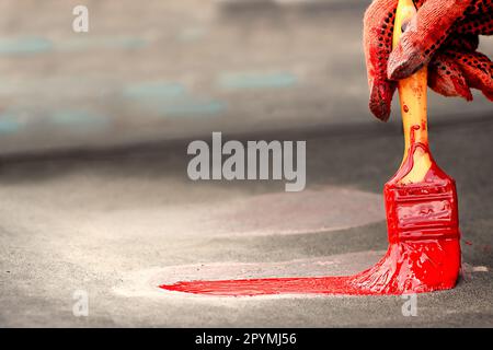 une personne tient une brosse avec de la peinture rouge, dessine une empreinte des chaussures d'enfants, sur la surface, sur le terrain de jeu, sa main est protégée par un gant spécial Banque D'Images