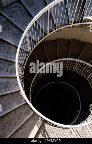 Un escalier en spirale en béton et en métal descendant dans un puits d'escalier sombre. Banque D'Images