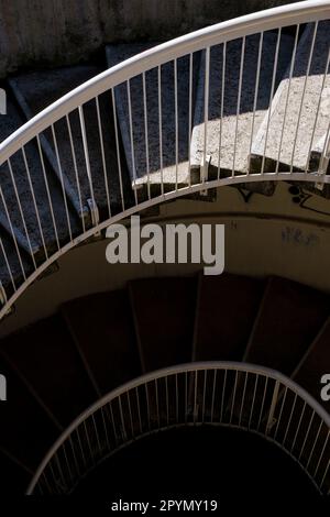 Un escalier en spirale en béton et en métal descendant dans un puits d'escalier sombre. Banque D'Images