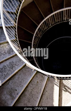 Un escalier en spirale en béton et en métal descendant dans un puits d'escalier sombre. Banque D'Images