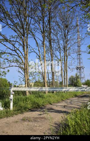 Sentier de terre avec une barre au début de celle-ci et un mât radio en arrière-plan derrière les arbres lors d'une journée ensoleillée dans la campagne italienne Banque D'Images