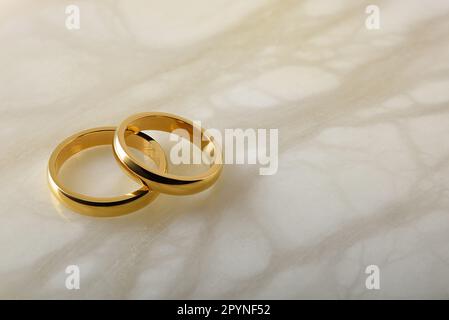 Détail de deux anneaux de mariage dorés l'un sur l'autre sur le marbre blanc. Vue en hauteur du dessus. Banque D'Images