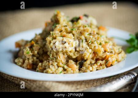 boulgour cuit avec des légumes, des carottes et des champignons séchés dans une assiette sur une table en bois. Banque D'Images