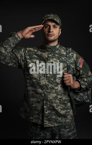 Soldat patriotique en uniforme avec le drapeau américain saluant isolé sur noir, image de stock Banque D'Images