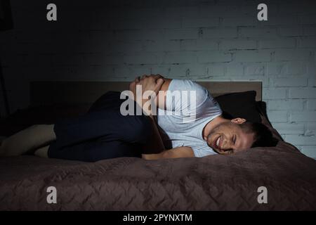 jeune homme aux yeux fermés souffrant de trouble de stress post-traumatique en étant allongé sur le lit la nuit, image de stock Banque D'Images