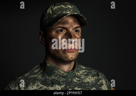 soldat avec de la saleté sur le visage debout en uniforme et la casquette souffrant de ptsd isolé sur gris, image de stock Banque D'Images