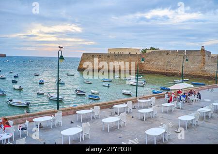 Plage de la Caleta avec dîner en plein air, petits bateaux sur les vagues et château médiéval de Santa Catalina en arrière-plan, Cadix, Espagne Banque D'Images