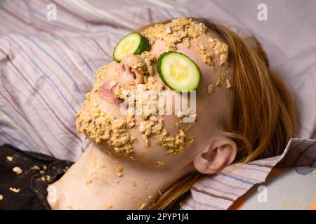 Une femme fait un masque cosmétique à la maison à partir de flocons d'avoine sur son visage et concombre.Traitements anti-âge, concept de soins de la peau. Banque D'Images