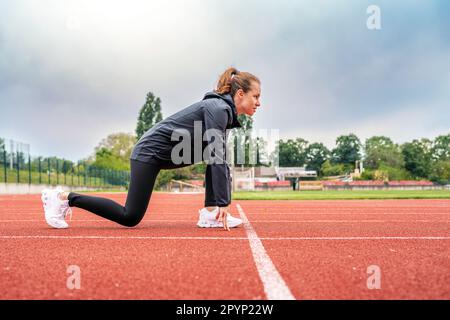 Jeune femme en position de départ sur la piste de course pendant l'exercice. Banque D'Images