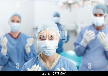 Notre travail est de la plus haute importance. Portrait de quatre chirurgiens tenant leurs mains en portant des gants de protection blancs et des masques faciaux. Banque D'Images