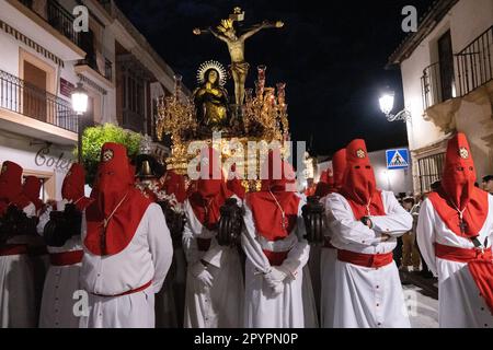 Nazarenos portant des capots rouges portent une plate-forme massive avec une statue de Jésus-Christ pendant la procession silencieuse de minuit commençant le Vendredi Saint à la semaine Sainte ou Semana Santa, 6 avril 2023 à Ronda, Espagne. Ronda, établie pour la première fois au 6th siècle avant Jésus-Christ, organise des processions de la semaine Sainte depuis plus de 500 ans. Banque D'Images