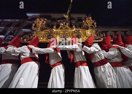 Nazarenos portant des capots rouges portent une plate-forme massive avec une statue de Jésus-Christ pendant la procession silencieuse de minuit commençant le Vendredi Saint à la semaine Sainte ou Semana Santa, 6 avril 2023 à Ronda, Espagne. Ronda, établie pour la première fois au 6th siècle avant Jésus-Christ, organise des processions de la semaine Sainte depuis plus de 500 ans. Banque D'Images