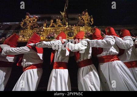 Nazarenos portant des capots rouges portent une plate-forme massive avec une statue de Jésus-Christ pendant la procession silencieuse de minuit commençant le Vendredi Saint à la semaine Sainte ou Semana Santa, 6 avril 2023 à Ronda, Espagne. Ronda, établie pour la première fois au 6th siècle avant Jésus-Christ, organise des processions de la semaine Sainte depuis plus de 500 ans. Banque D'Images