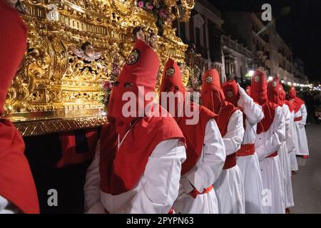 Nazarenos portant des capots rouges portent une plate-forme massive avec une statue de Jésus-Christ pendant la procession silencieuse de minuit commençant le Vendredi Saint à la semaine Sainte ou Semana Santa, 6 avril 2023 à Ronda, Espagne. Ronda, établie pour la première fois au 6th siècle avant Jésus-Christ, organise des processions de la semaine Sainte depuis plus de 500 ans. Banque D'Images