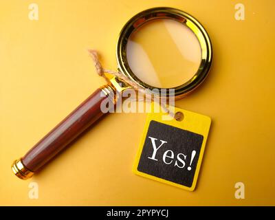 Loupe et panneau en bois avec le mot Oui sur fond jaune Banque D'Images