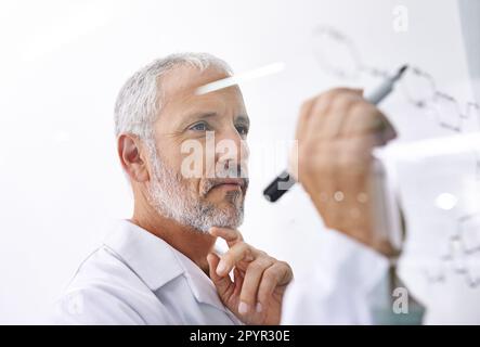 Analyse des liaisons chimiques. un scientifique mâle mature dessinant une structure moléculaire sur une surface en verre. Banque D'Images