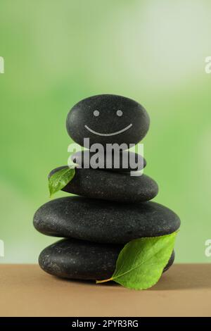 Pile de pierres avec visage heureux dessiné et feuilles vertes sur la table sur fond flou. Concept Zen Banque D'Images