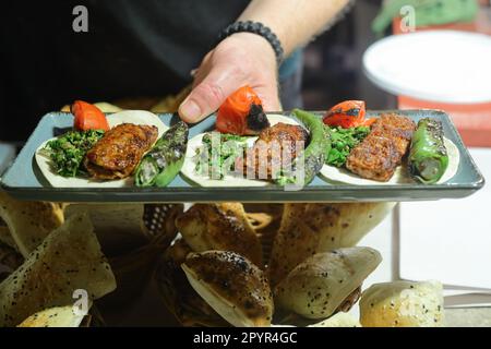 Une assiette avec un shish et un kebab adana dans les mains d'un gros plan de cuisson Banque D'Images