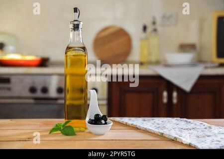 Bouteille d'huile de cuisson, olives et basilic sur table en bois dans la cuisine, espace pour le texte Banque D'Images