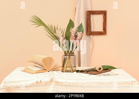 Vase avec ananas décoratif, feuilles de palmier, livre et corde sur la table près du mur beige Banque D'Images