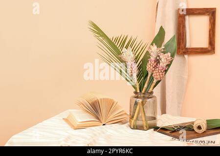 Vase avec ananas décoratif, feuilles de palmier, livre et corde sur la table près du mur beige Banque D'Images
