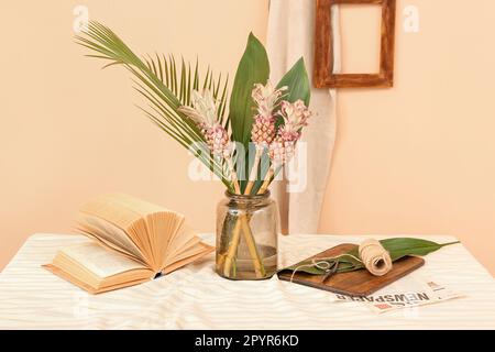 Vase avec ananas décoratif, feuilles de palmier, livre et corde sur la table près du mur beige Banque D'Images