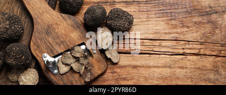 Rasoir avec truffes noires entières et tranchées sur une table en bois, plat avec espace pour le texte. Bannière Banque D'Images