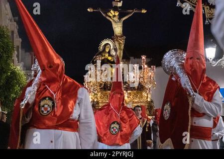 Les Cofradias portant des capuches en forme de cône rouge mènent une plate-forme géante avec la Crucifixion pendant la procession silencieuse de minuit marquant le Vendredi Saint à la semaine Sainte ou le Père Noël Semana, 6 avril 2023 à Ronda, Espagne. Ronda, établie pour la première fois au 6th siècle avant Jésus-Christ, organise des processions de la semaine Sainte depuis plus de 500 ans. Banque D'Images