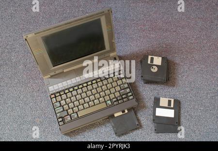 mains d'une personne prenant une disquette et la plaçant dans un vieil ordinateur portable. La personne est sur le sol d'une pièce Banque D'Images