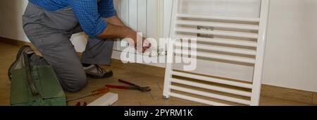 Image d'un plombier dans une maison qui monte des radiateurs avec une clé. Installation de chauffage pour une maison. Bannière horizontale Banque D'Images