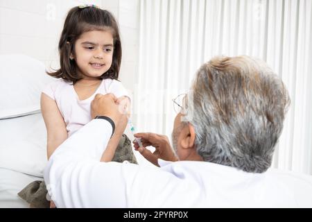 Un pédiatre indien senior effectue une vaccination d'une petite fille. Médecin administrant une injection à une femme enfant dans une clinique. Injection de syr Banque D'Images