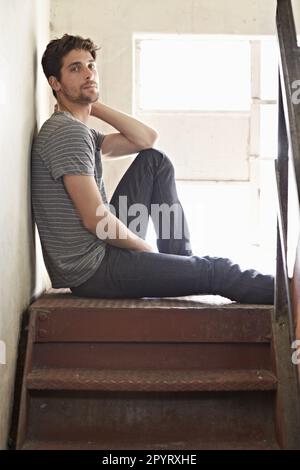 Portrait, dépression et solitaire avec un homme sur un escalier dans sa maison, assis sur l'atterrissage par une fenêtre. Seul, la santé mentale et se détendre avec un Banque D'Images