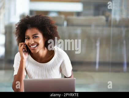 Le multitâche à l'ère moderne. Portrait d'une jeune femme attrayante parlant au téléphone tout en utilisant un ordinateur portable. Banque D'Images