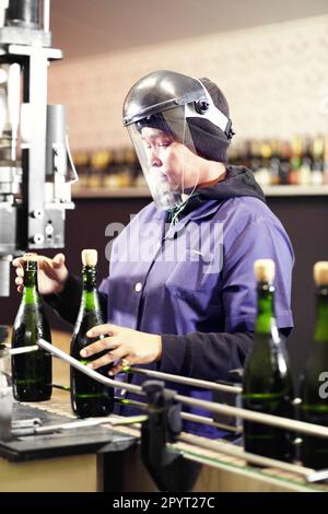 Alcool, bouteille de vin et femme travaillant dans une distillerie ou une usine industrielle. L'équipement, les bouteilles en verre et la femme travaillant avec un epi travaillent sur le rouge Banque D'Images