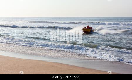 Le bateau à requins et l'équipage d'entretien non identifié débarque à travers les vagues de l'océan sur le sable de la plage tôt le matin après avoir vérifié les filets de bain . Banque D'Images