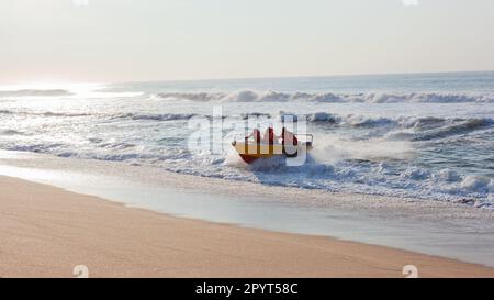 Le bateau à requins et l'équipage d'entretien non identifié débarque à travers les vagues de l'océan sur le sable de la plage tôt le matin après avoir vérifié les filets de bain . Banque D'Images