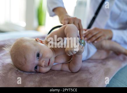 Jeune médecin pédiatre examinant mignon petit bébé allongé sur le côté dans le bureau et regardant dans l'appareil photo Banque D'Images