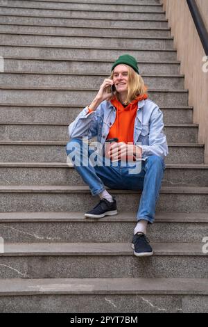 Joyeux boxeur millénaire parlant au téléphone tout en étant assis sur les escaliers pour piétons Banque D'Images