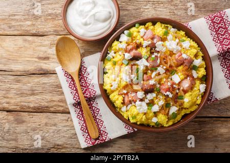 Cuisine ukrainienne porridge de maïs avec oignon, crépitements et fromage sur le bol sur la table en bois. Vue horizontale du dessus Banque D'Images