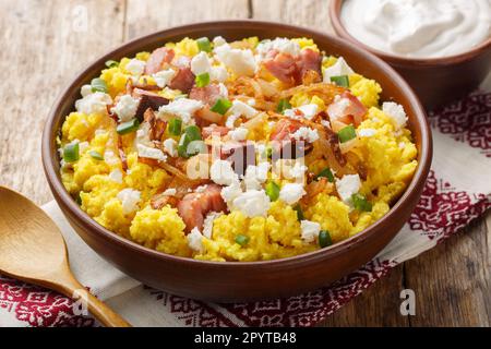 Porridge de maïs servi avec du fromage, des oignons frits et du bacon sur le bol de la table en bois. Horizontale Banque D'Images