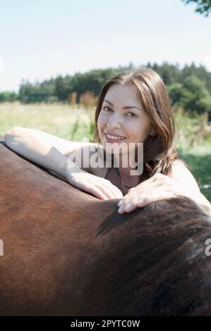 Portrait d'une femme mûre penchée sur le dos de son cheval brun et souriante, Bavière, Allemagne Banque D'Images