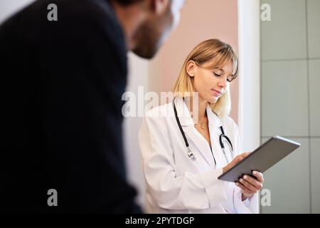 Femme blonde médecin utilisant un PC de tablette par un patient mâle dans la clinique Banque D'Images