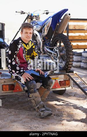 Prêt à tout affronter. Portrait d'un jeune coureur de moto de terre assis sur une remorque avec son vélo. Banque D'Images