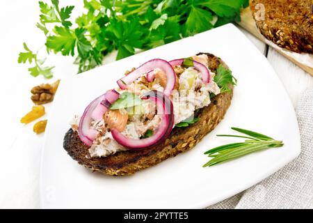 Salade de saumon, de céleri de petite taille, de raisins secs, de noix, d'oignons rouges et de fromage cottage sur du pain grillé avec de la laitue verte sur une assiette contre du bois léger b Banque D'Images