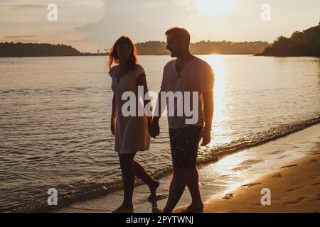 couple romantique marchant sur la plage, vacances de lune de miel, silhouettes d'homme et de femme tenant les mains Banque D'Images