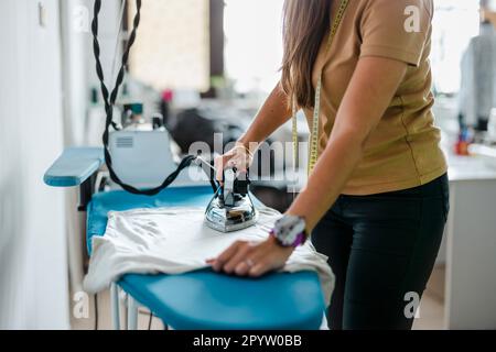 Femme utilisant un fer à repasser en se tenant dans un studio de couture Banque D'Images