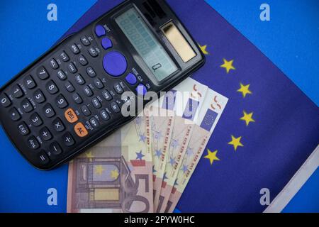 Le drapeau de l'Union européenne placé sur fond bleu, des euros et une calculatrice. photographié d'en haut. Banque D'Images