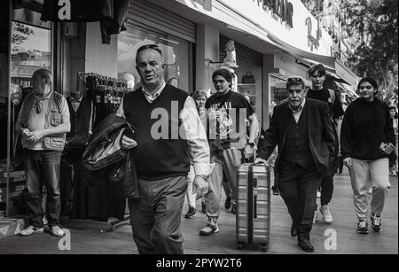 Un homme âgé vêtu d'un costume pousse une valise le long de laquelle d'autres Turcs marchent dans une rue commerçante animée d'Antalya, province d'Antalya, Turquie ( Banque D'Images