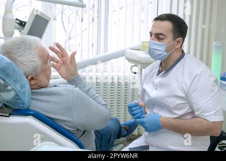L'homme principal assis dans une chaise de dentiste parle de ses problèmes dentaires au médecin Banque D'Images