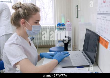 Assistant dentiste travaillant sur un ordinateur portable dans un cabinet dentaire portant des gants et un masque médicaux Banque D'Images